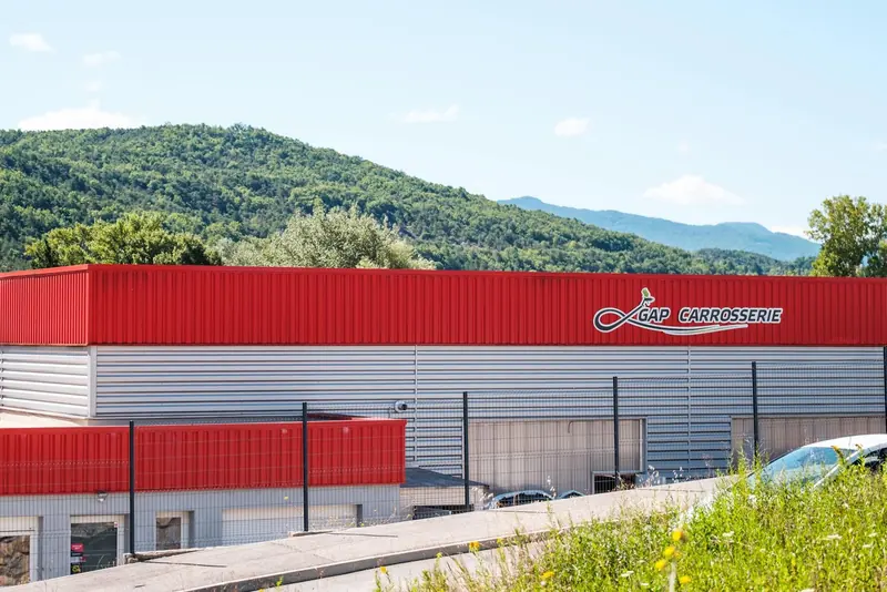 L’atelier Arena Gap Carrosserie, un bâtiment rouge et gris, devant les montagnes