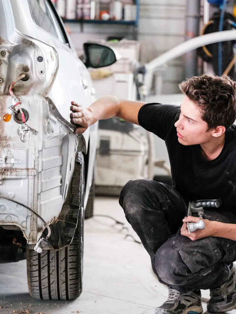 Un carrossier examine de près la carrosserie abîmée d’une voiture grise