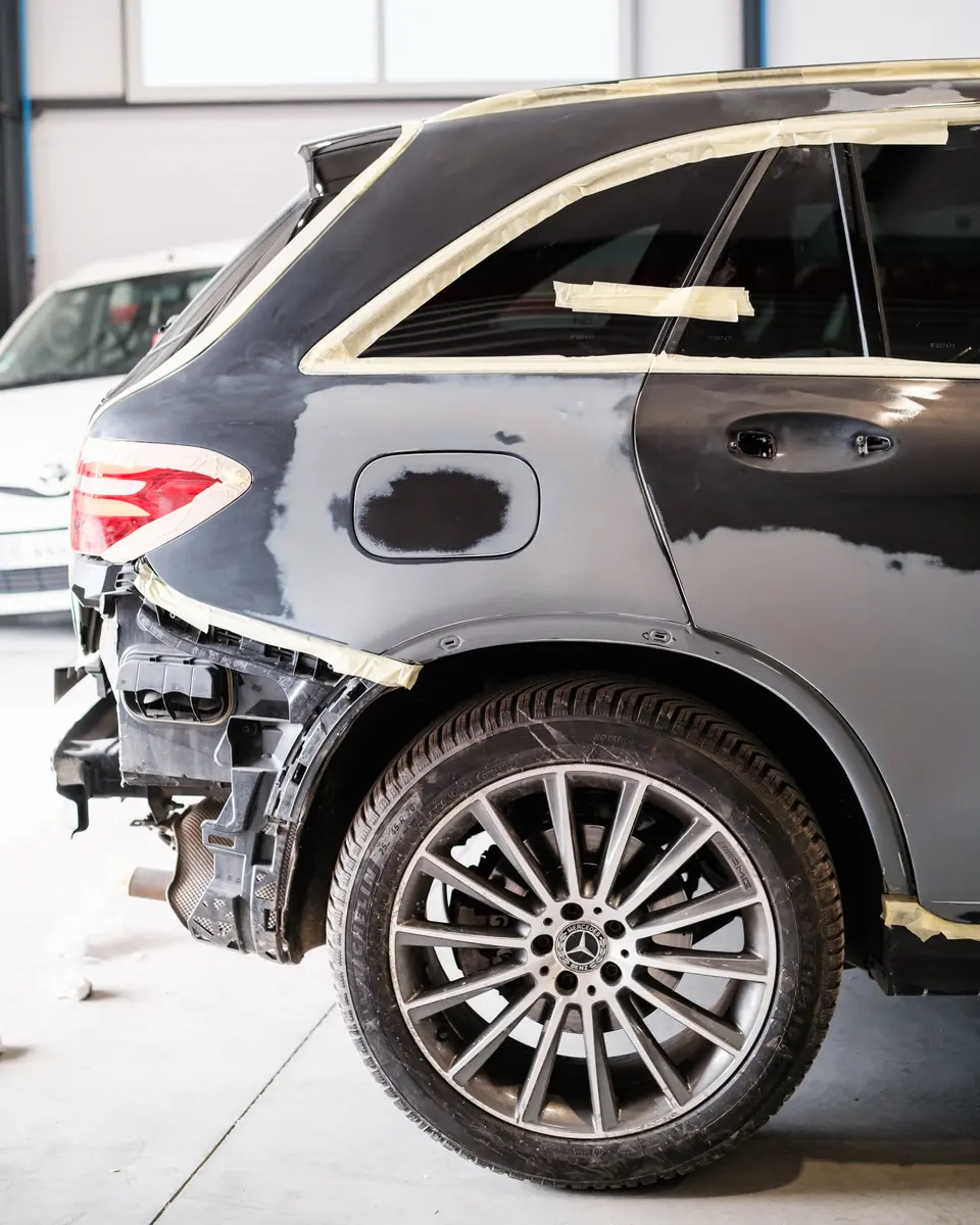 L’arrière d’une Mercedes grise en réparation, protégé par du ruban de masquage