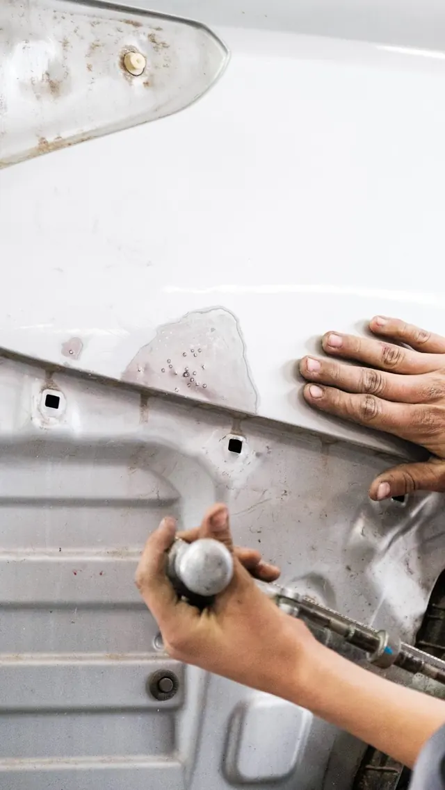 Des mains redressent la tôle d’une voiture blanche