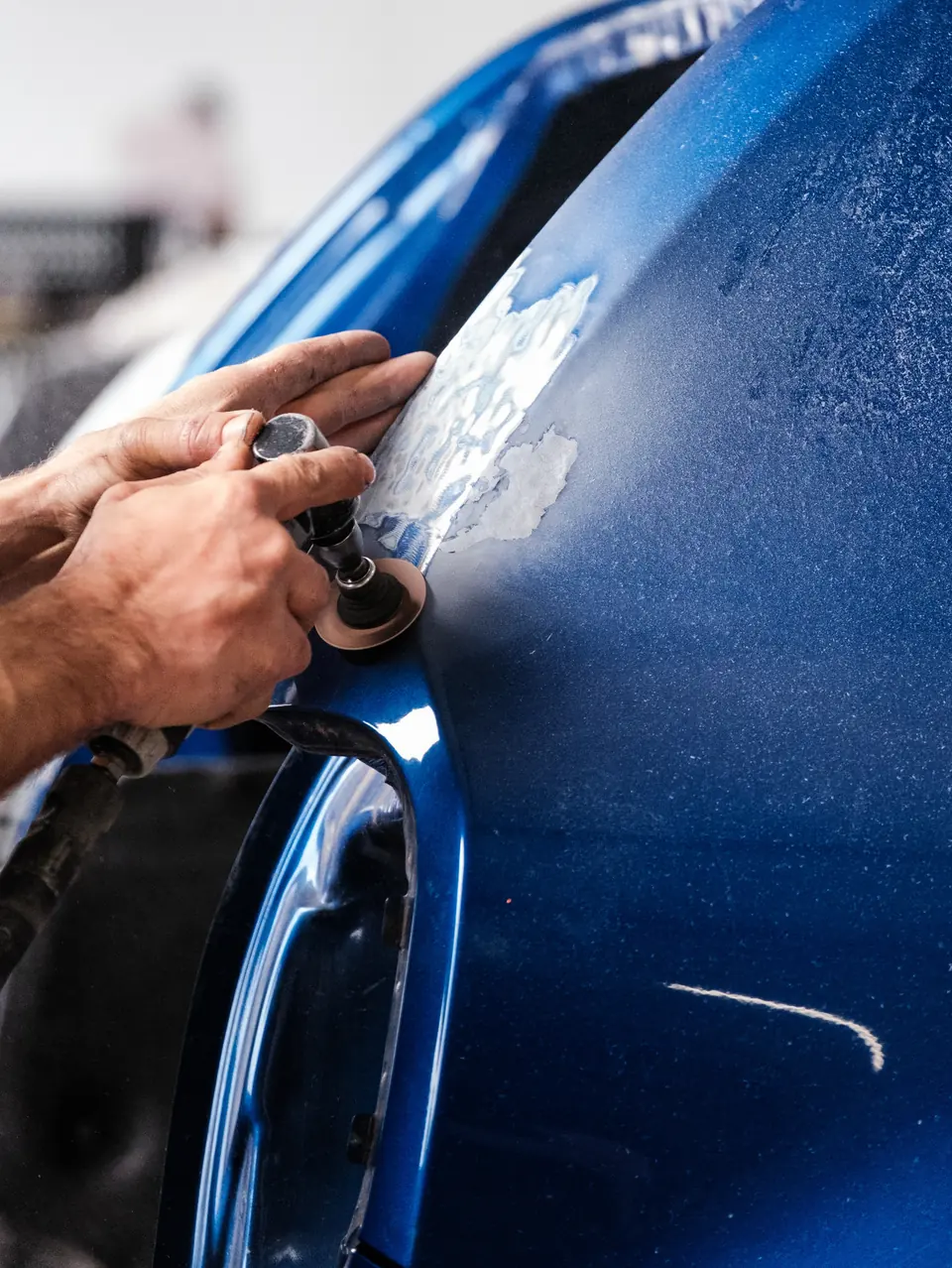 Une ponceuse efface des rayures sur l’aile d’une voiture bleue